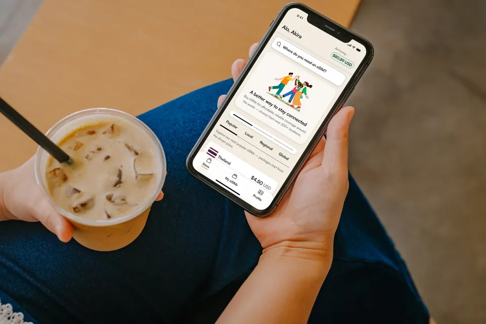 A hand holding a phone with the Airalo app open beside an iced coffee