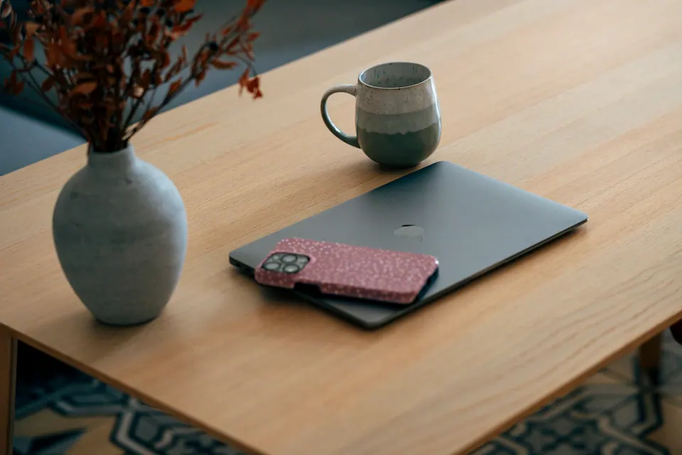 A closed laptop, phone and white mug on a wooden table