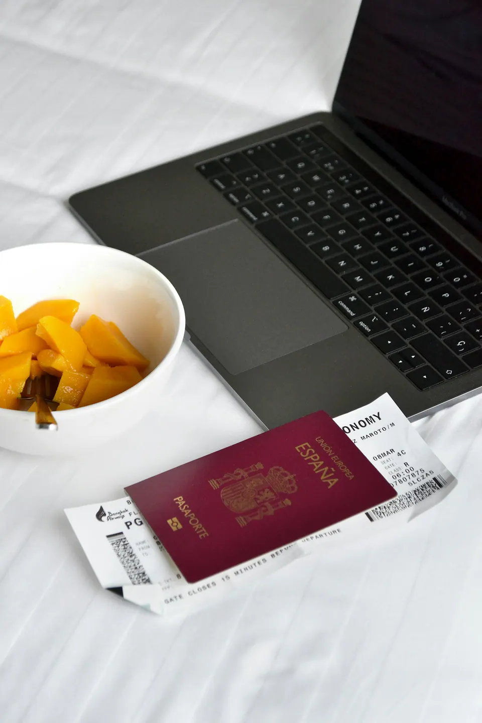 A laptop, passport and boarding pass beside a breakfast plate