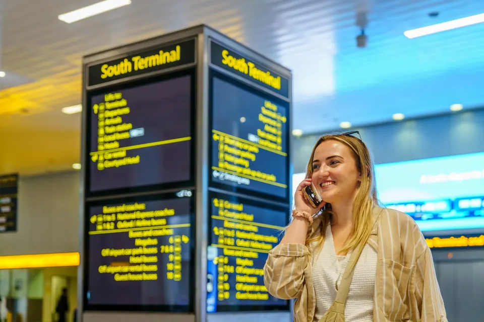 A traveler talking on a phone beside Gatwick South Terminal departure signs