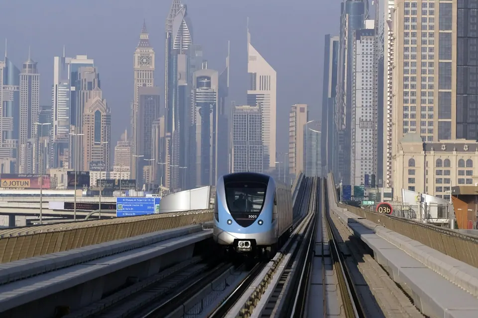 A Dubai Metro train approaching with city towers behind it