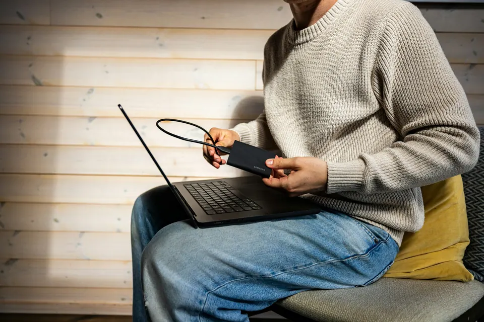 A person holding a portable storage drive beside an open laptop
