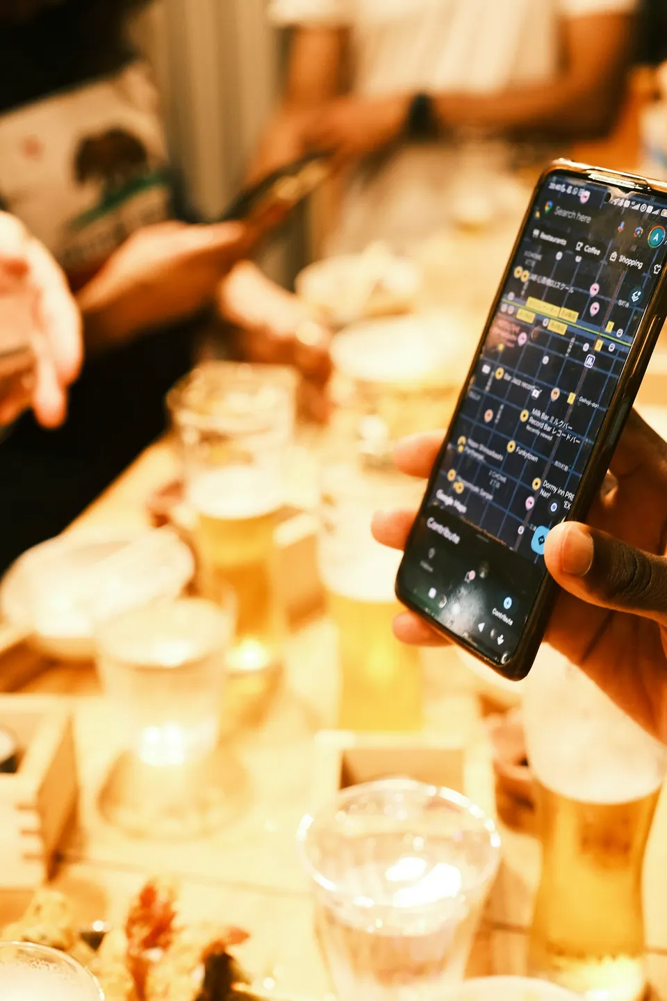 A person holding a phone with a map open above a table with drinks