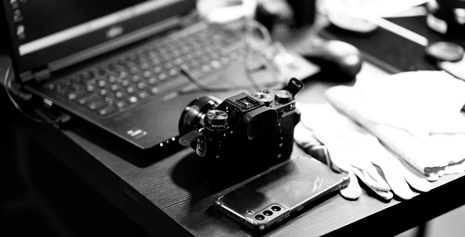 A camera, phone and laptop arranged together in black and white