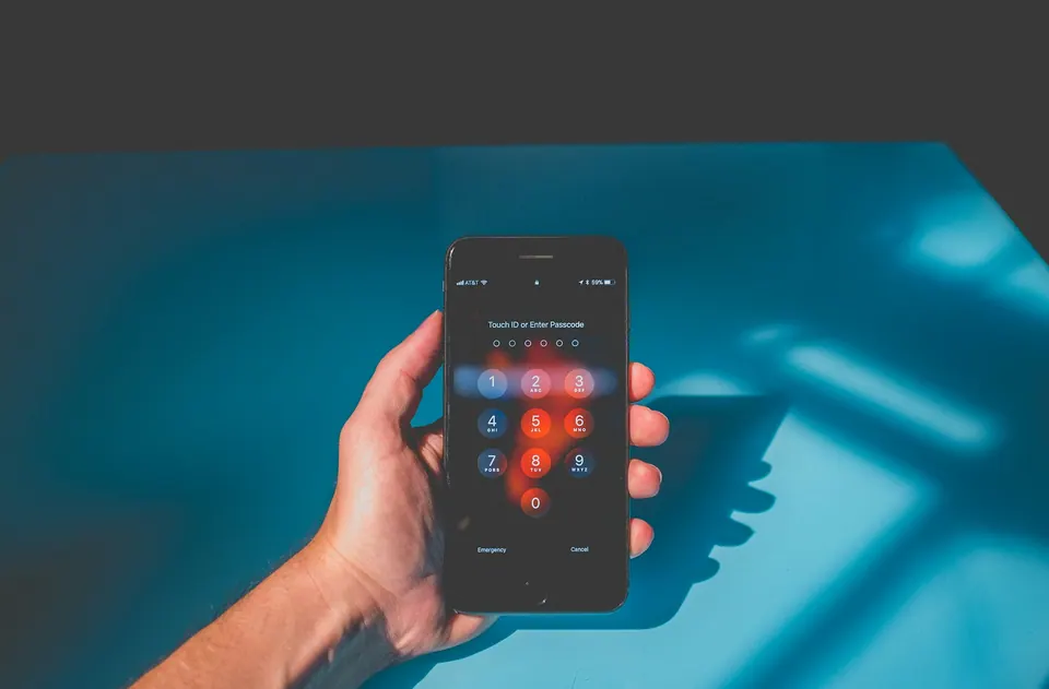 A hand holding an iPhone with its passcode keypad against a blue background