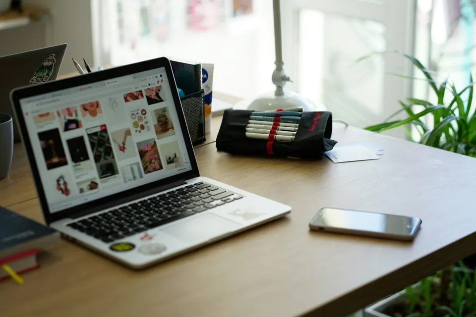 A phone beside an open laptop on a wooden table with plants behind it