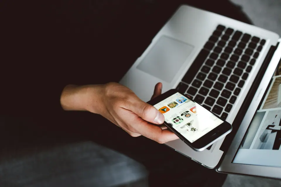 A person holding a phone above an open laptop on their lap