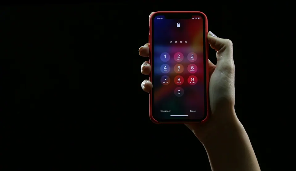 A hand holding a red-cased iPhone at its passcode keypad