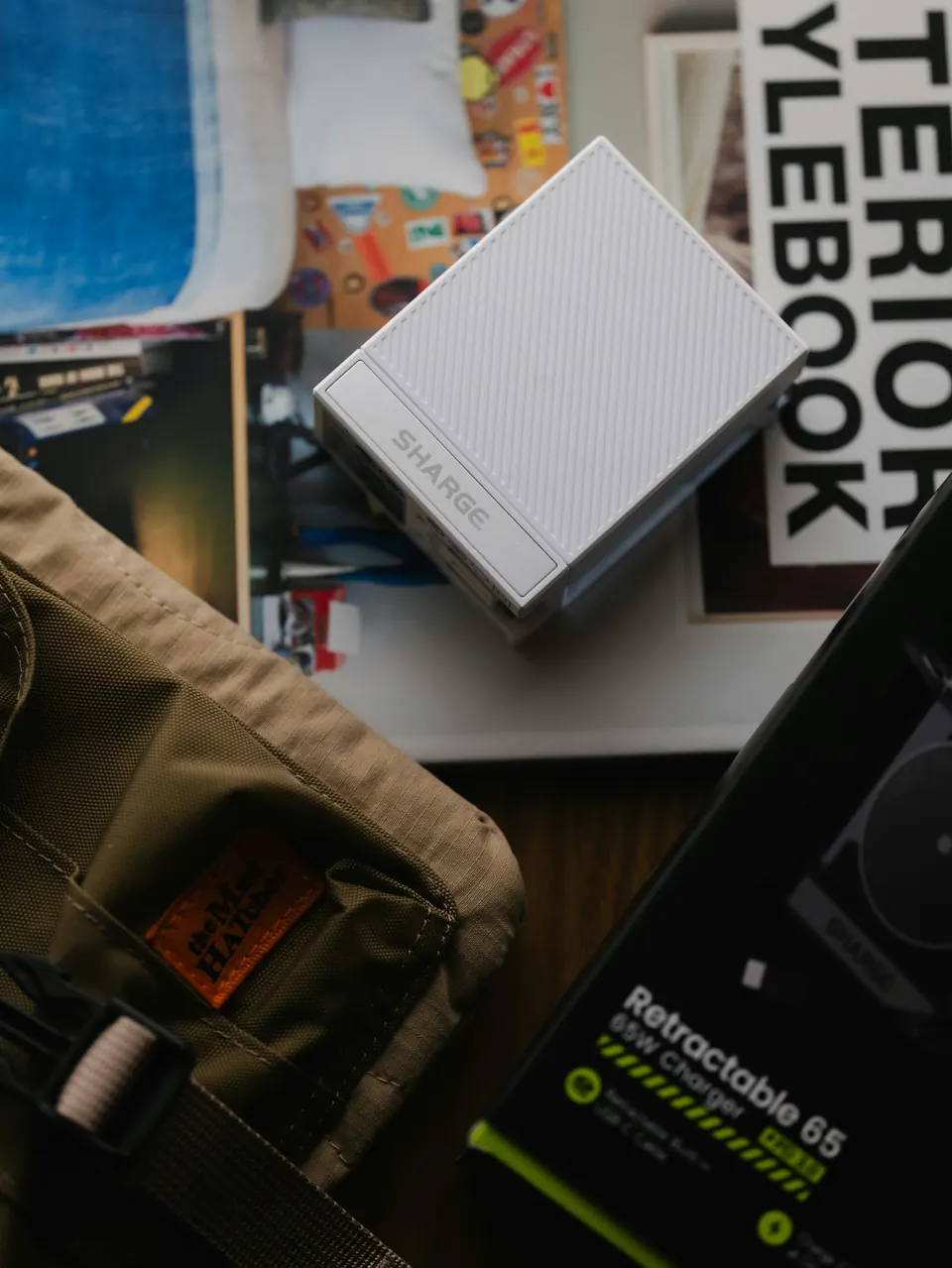 A white portable charger on magazines beside a cable box and small bag