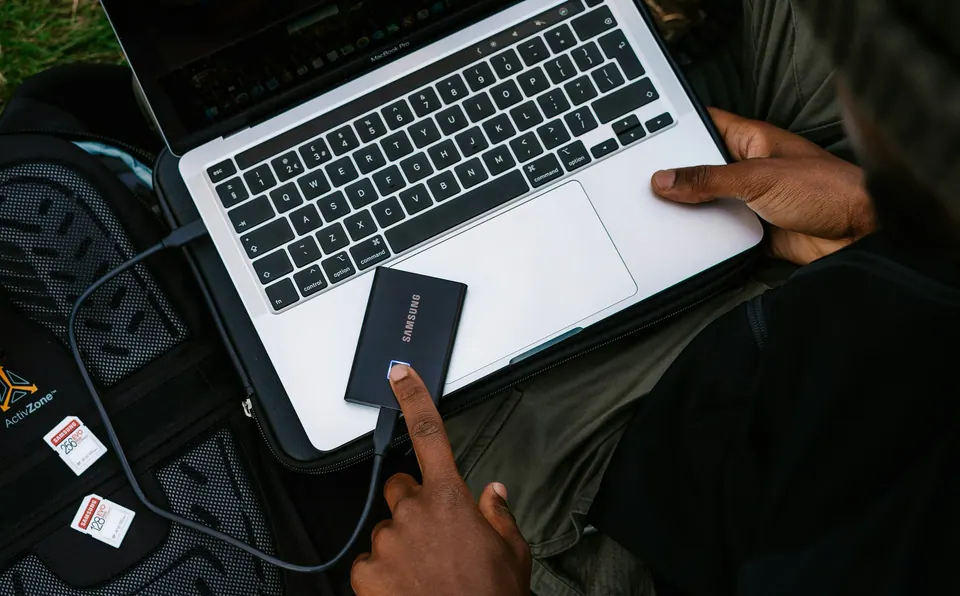 A portable Samsung SSD beside a laptop and a photographer’s equipment bag