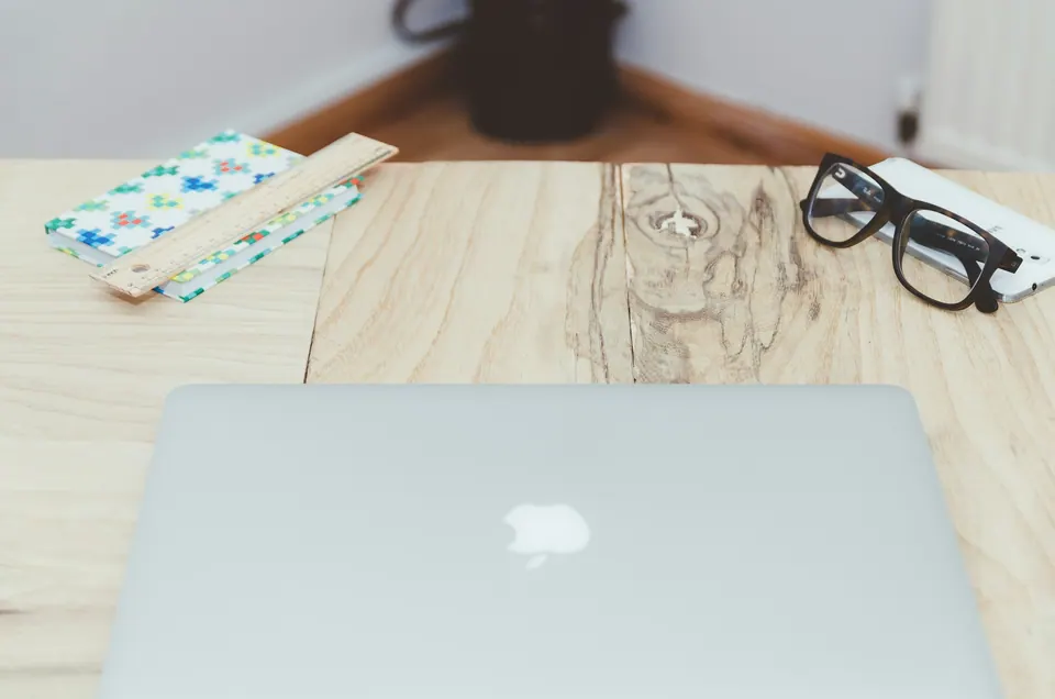 A closed laptop, notebook and glasses on a light wooden table