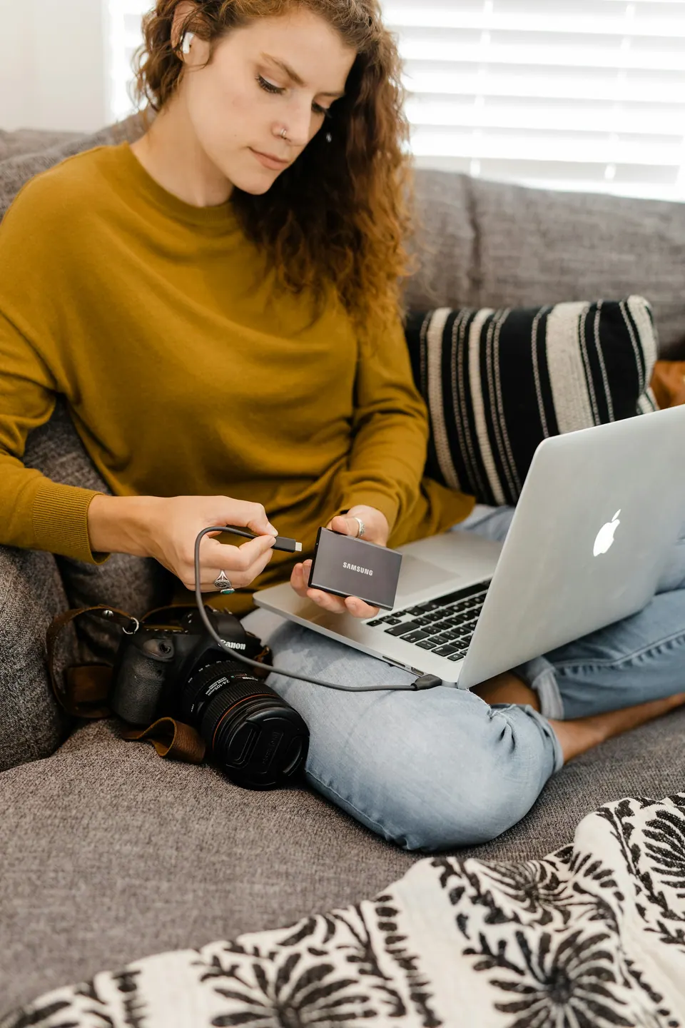 A person holding a portable SSD beside an open laptop and camera