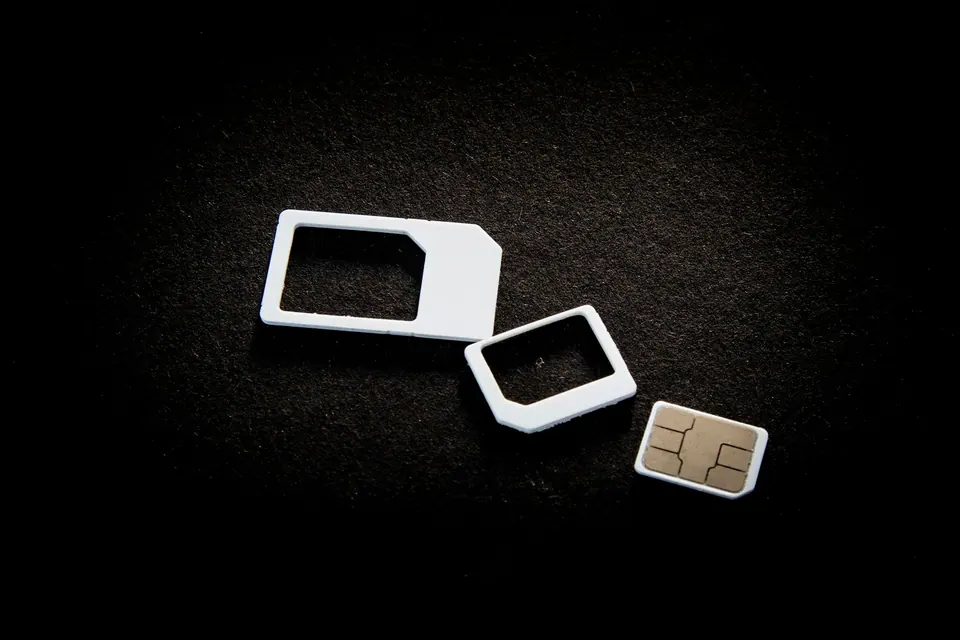 A SIM card beside two different-size SIM adapters on a dark surface