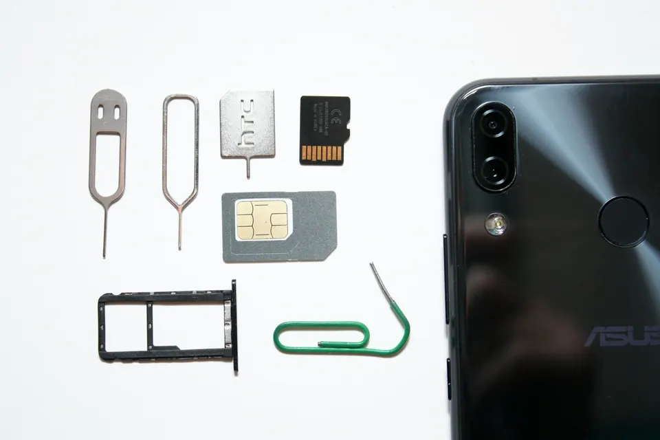 A phone, SIM tray, ejector tools and cards on a white surface