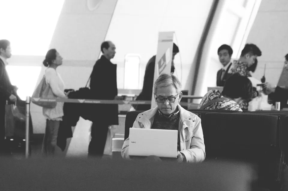 A traveler using a laptop at an airport lounge table in black and white