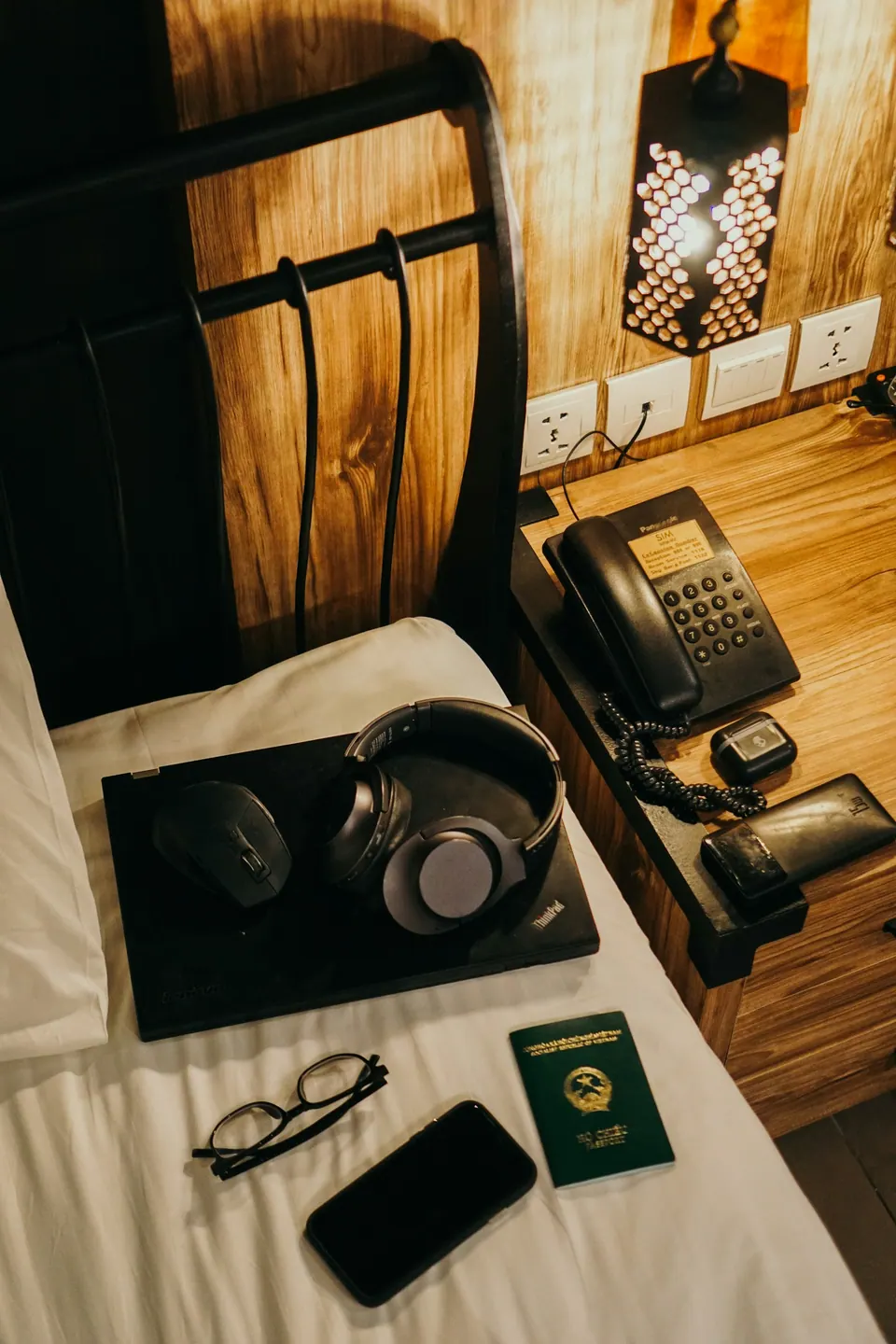 A phone, passport and headphones arranged on a hotel bed beside a room telephone