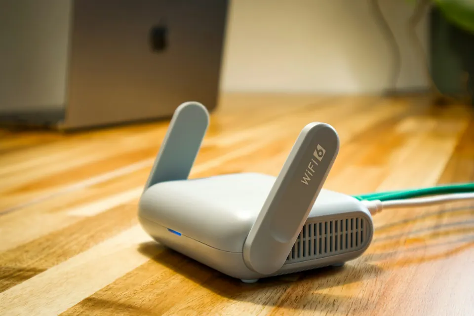 A compact two-antenna Wi-Fi router with connected cables on a wooden desk