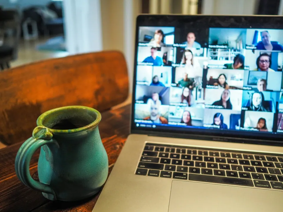A laptop displaying a multi-person video meeting beside a mug
