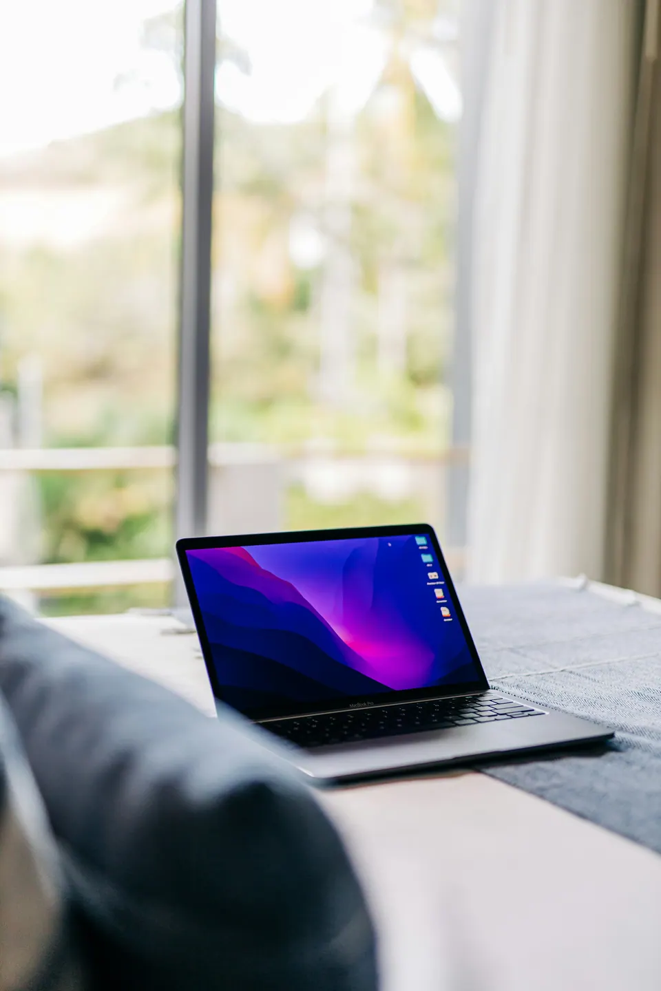 An open laptop on a cushioned seat beside a bright window