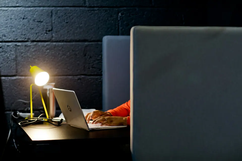 A person using a laptop in a sheltered coworking booth lit by a desk lamp