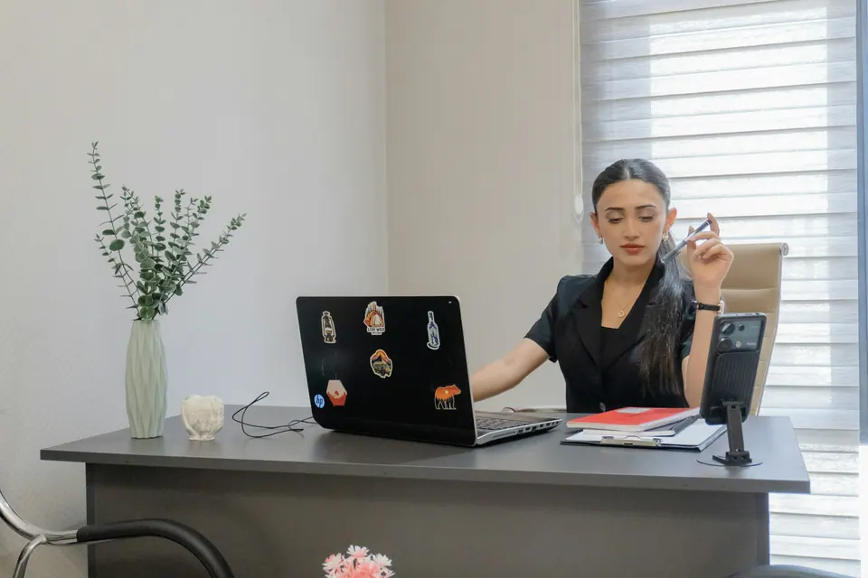 A person at a desk with an open laptop and a phone on a stand